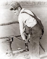Photo of young Tom Spencer pumping water using a hand pump.